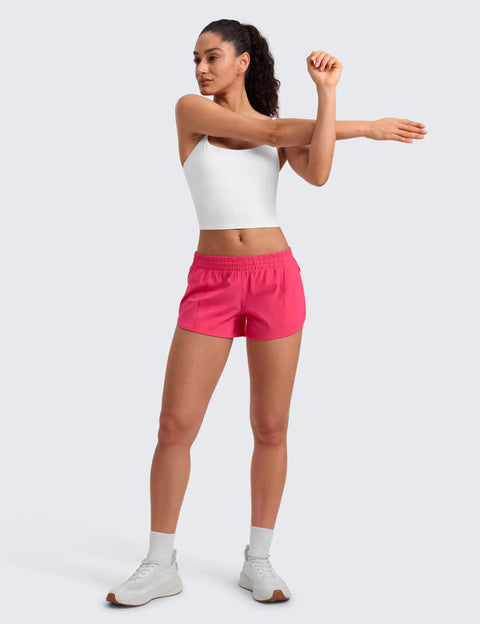 Woman stretching in Low Waisted Running Shorts 2.5 Inch Inseam In Lip Gloss Pink With Built-In Mesh Liner, Friction-Reducing, Side Zip Pocket