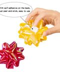 Hand holding self-adhesive yellow bow from 100 Pcs Bright Bows And Ribbon Assortment Set For Gift Wrapping with red bow beside