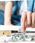 Person holding a carbon steel binding screw above scattered fasteners, showcasing silver finish and no sweat twist lock system.