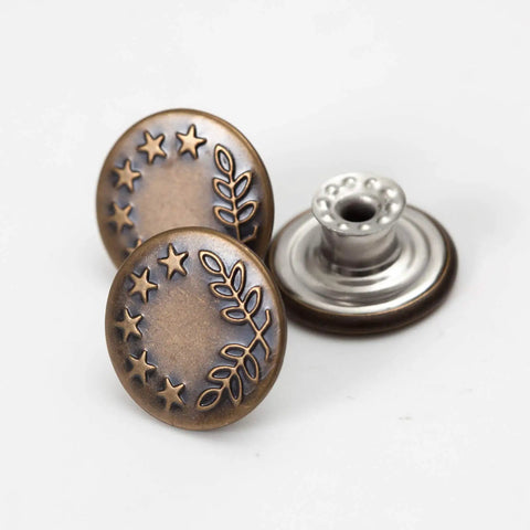 Close-up of 20 Sets Of 17mm Replacement Jeans Buttons Snap Kit With Metal Rivets For Jeans Denim Pants No Sew Button Replacement Durable Riveted Button Set For Quick Fixes, showing bronze decorative pattern and silver base.