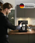 Sleek Fully Automatic Coffee And Espresso Machine With Silent Steel Grinding Chamber For Killer Cup Creations and Rich Silky Milk Foam For Serious Home Baristas, operated by a man in a kitchen.