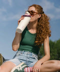 Person drinking from FreeSip 2-In-1 Spout Water Bottle with Built-In Straw and Bucket Handle, outdoors, focusing on insulated stainless steel design.