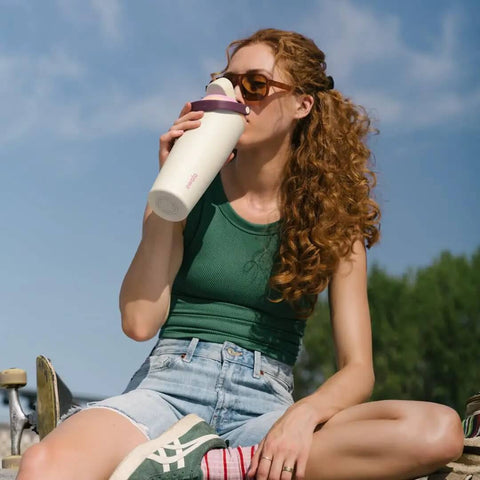 Person drinking from FreeSip 2-In-1 Spout Water Bottle with Built-In Straw and Bucket Handle, outdoors, focusing on insulated stainless steel design.