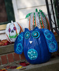 Outdoor Halloween pumpkins decorated with a blue duct tape owl and two colorful pumpkin designs on a porch.