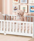 Full Size Floor Bed With Fence And Door For Toddlers And Kids in a nursery, with safe guardrails, wooden platform, white finish, teddy bear on bed
