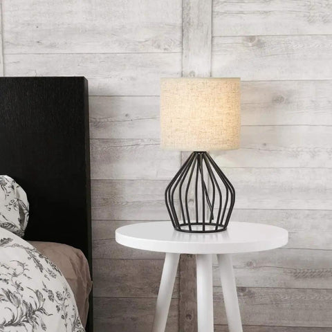 Black Modern Table Lamp With Linen Fabric Shade And Hollowed Base on white nightstand in bedroom.