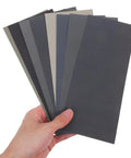 Hand holding 56 Piece Wet And Dry Sanding Sheets Kit With Assorted Grit 400 To 5000 For Wood And Metal Carborundum Kraft Paper