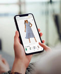 Person shopping online for a blue dress on a smartphone screen, with hand holding the phone and swiping through options.