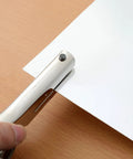 Person using Beefy Heavy Duty 1/8 Inch Single Hole Punch with ultra long depth up to 53mm on a piece of paper on a wooden table.