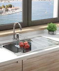 Modern kitchen sink with a stainless steel faucet and countertop, overlooking a scenic water view through large windows.