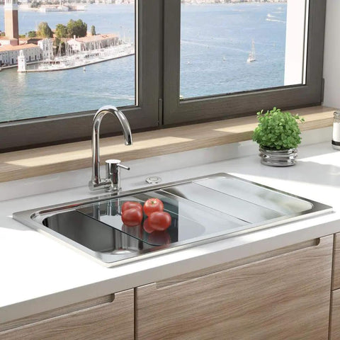 Modern kitchen sink with a stainless steel faucet and countertop, overlooking a scenic water view through large windows.