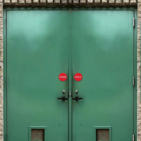 Two Inch Round Push Pull Door Signs Brushed Gold Set Of Two Durable Plastic With Strong Adhesive Foam Tape For Super Easy Install And Clear Legible Messaging In Offices Homes Or Commercial Doors, shown on green double doors