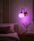 BOKT Ribbed Glass Battery Operated Wall Sconce Set of 2 with 12 RGB Colors illuminated in purple beside a bed.