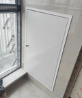 Massive Aluminum Access Panel For Drywall Flush Mount Inspection Door With Heavy Duty Latch Rustproof White Finish installed beside a window.