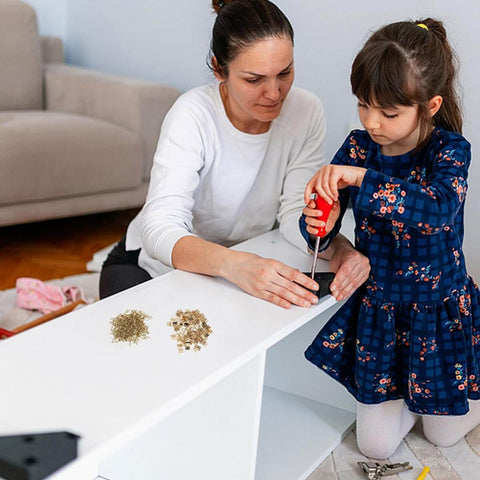 Adult and child assembling furniture with screws and hinges on a white board.