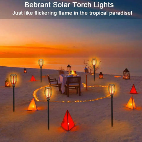 Beach sunset with 43 Inch Solar Torch Lights With Realistic Flickering Flames lighting a dinner setup, outdoor decor