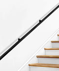 Heavy Duty Wall Mounted Handrail For Indoor Stairs Featuring An Extra Long Eleven Foot Black Steel Rail Built Tough For Rock Solid Grip And Keeps You Standing Tall on white wall above wooden stairs.