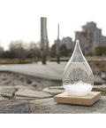 Teardrop crystal Storm Glass Weather Predictor with wood base on stone ledge, modern weather station for home or office decor.