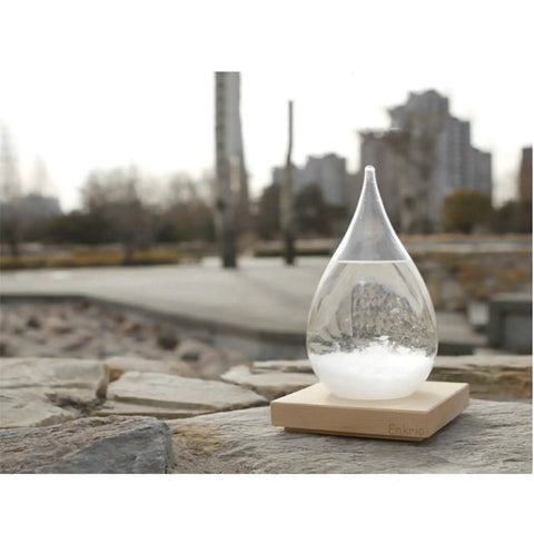 Teardrop crystal Storm Glass Weather Predictor with wood base on stone ledge, modern weather station for home or office decor.