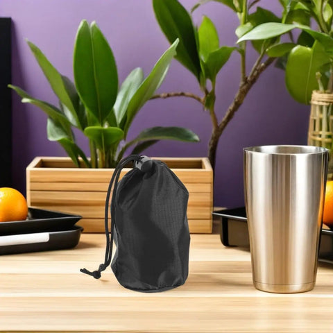 Two Pack Waterproof Rain Gear Storage Bags With Drawstring Pouches For Quick Access Rain Poncho Organizer For Cycling Hiking Camping And Travel next to a metal cup on a wooden table with plants in the background.