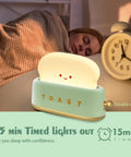 Woman sleeping next to Rechargeable Cute Toaster Lamp With Smile Face, Adorable Night Light Desk Decor, and an alarm clock.