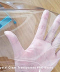 Hand holding crystal clear round vinyl tablecloth for 22 to 26 inch tables heavy duty elasticized fit with elastic edges