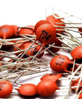 Close-up of ceramic capacitors from the Ceramic Capacitor Assortment Kit DIP 2pF To 100nF 30 Values 10 Pieces Each 300 Pieces Total 50V Rating Individually Bagged DIY Friendly For Prototyping And Hobby Electronics, showing orange components and metal leads.