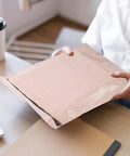 Person holding khaki PE mailer with strong glue and easy seal, waterproof packaging bag for clothes and cosmetics 100 pack.