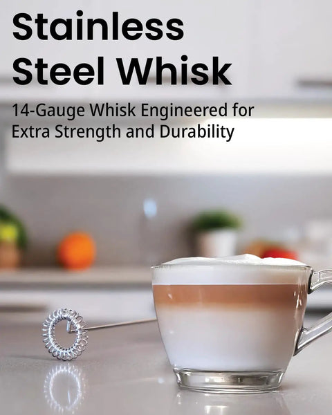 Stainless steel frother whisk next to a cappuccino cup on a kitchen counter, used for barista-style foam and mixing.