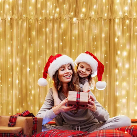 9.8 By 9.8 Feet 300 LED Curtain Lights With USB Plug illuminating a festive scene with two people wearing Santa hats indoors.
