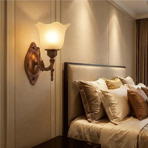 Antique Copper Wall Sconce Light European Vintage Design with Flower Glass Shade Carved Base Indoor Wall Lamp for Bedroom Living Room Hallway Bedside Decor E26/27 next to a bed with plush pillows.