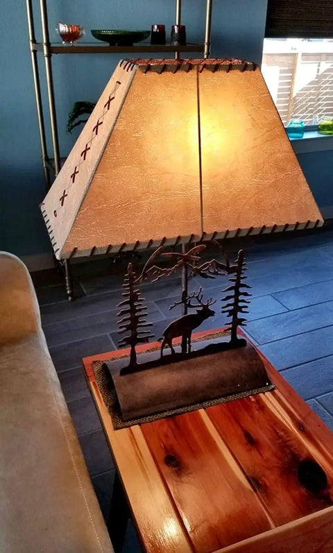 Rustic Elk Table Lamp With Faux Rawhide Shade, Inline Dimmer, 26 Inch Cabin Lighting For Living Room Or Den, Cozy Amber Glow, Durable Wood Base on a table.