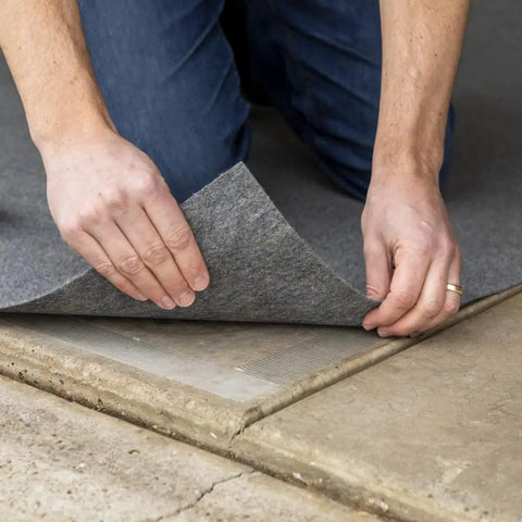 Hands laying carpet with Indoor Outdoor Carpet Tape One Point Four One Inch By Forty Two Feet White Fiberglass Reinforced Durable Adhesive.