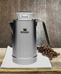 Hold Tight Percolator Coffee Pot 1.1 Qt Stainless Steel Six Cup Stove Top or Open Fire Coffee Maker, shown on table with coffee beans.