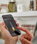 Person adjusting Indoor Smart Motion Sensor 2 Pack with Daylight Sensing settings on smartphone in kitchen.