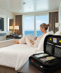 Black zippered travel medical kit opened on hotel nightstand, contents visible; woman reading on bed in background.