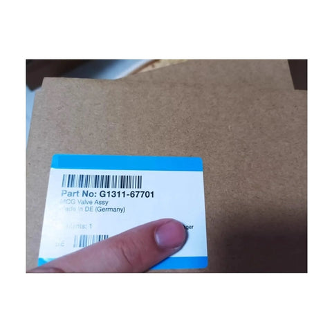 Front view of cardboard box for G1311-67701 electric proportional valve; blue top label with barcode, hand visible.