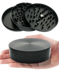 4-inch black zinc grinder for herbs and spices; 3-layer metal with sharp teeth, shown in hand for scale