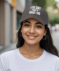 Smiling woman wearing a black cap with the text 'I Fix Shit That's What I Do' standing outdoors