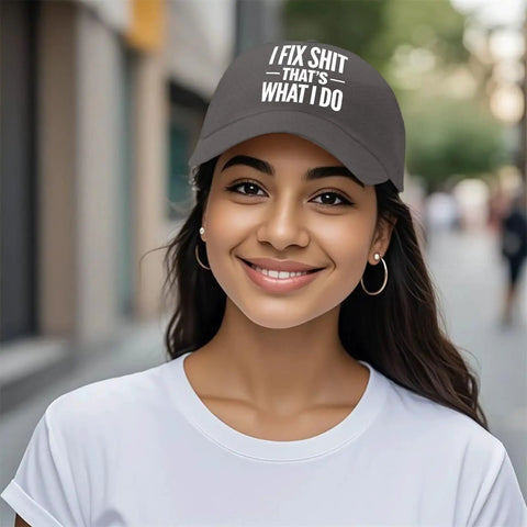 Smiling woman wearing a black cap with the text 'I Fix Shit That's What I Do' standing outdoors