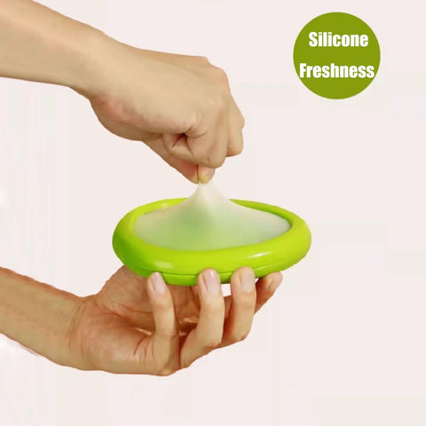 Hand stretching green silicone top, part of Set Of Four Reusable Fruit And Veggie Savers For Keeping Avocados Tomatoes Apples Garlic And Onions Fresh Longer In The Fridge Space Saving Design Makes Kitchen Organization Easy