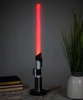 Darth Vader LED Lightsaber Lamp 24 Inch Tall Desk Night Light Star Wars Decor Red Blade Standing Light For Home Office Bedroom Mood Lighting Geeky Collectible Gift For Fans on a marble surface next to books and a plant.