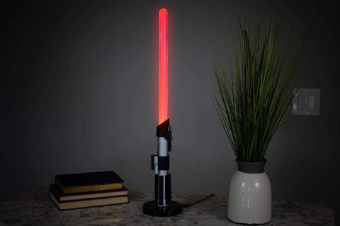 Darth Vader LED Lightsaber Lamp 24 Inch Tall Desk Night Light Star Wars Decor Red Blade Standing Light For Home Office Bedroom Mood Lighting Geeky Collectible Gift For Fans on a marble surface next to books and a plant.