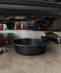 Huge 7 Qt Oil Drain Pan With Built Scale, Leak Proof Spout And Splash Guard placed under a car in a garage.