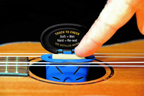 Humilele Ukulele Humidifier With Anti Drip Sponge Secures Between Strings And Fits All Sound Holes Keeps Your Ukulele Humidity Between Forty And Fifty Five Percent No Mess Water Reservoir That Holds Ten Times Its Weight. blue ukulele humidifier in sound hole being checked by finger