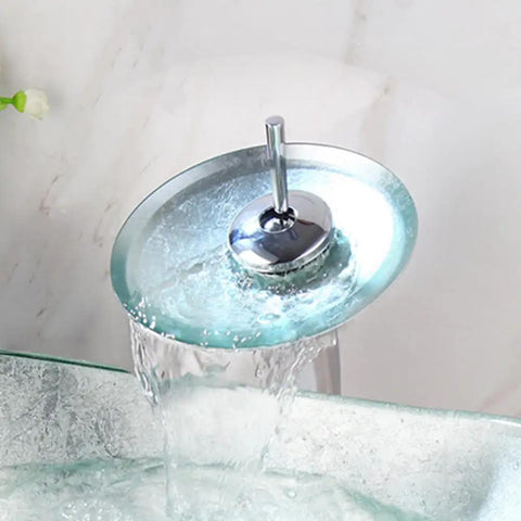 Water flow from chrome waterfall faucet of Dope Sleek Oval Glass Vessel Sink and Waterfall Faucet Combo With Pop Up Drain and Mounting Ring