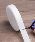 Heavy Duty White Sew On Hook And Loop Tape Nylon Fastener Strips 1 Inch By 33 Feet being cut with scissors on a wooden surface.