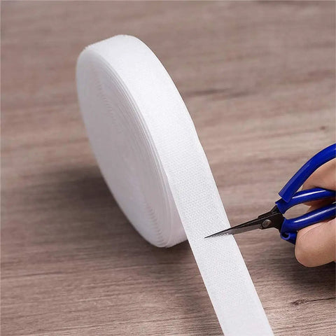 Heavy Duty White Sew On Hook And Loop Tape Nylon Fastener Strips 1 Inch By 33 Feet being cut with scissors on a wooden surface.