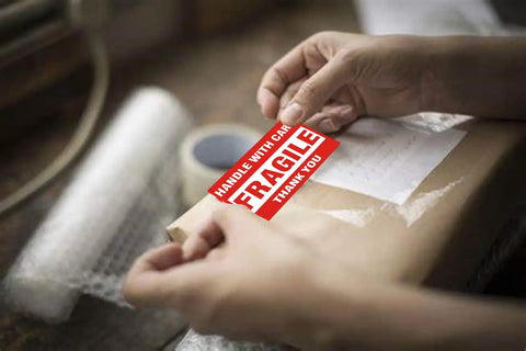 Person applying Handle With Care Fragile Shipping Labels 2 By 3 Inches Red Warning Pack Of 500 Per Roll Permanent Adhesive on package