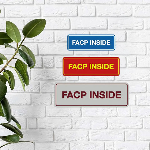Three FACP Inside Fire Safety Signs in blue, red, and white on a brick wall with a green plant on the left